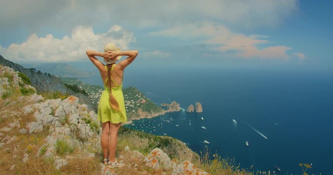 Woman standing on a rocky viewpoint of Monte Solaro overlooking Faraglioni cliffs and the wide blue sea of Capri Italy