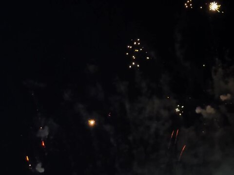 Bright golden and green fireworks exploding in the dark night sky during a festive celebration.