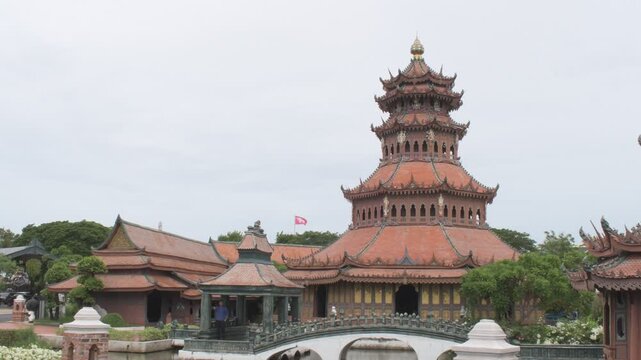 multi-tiered traditional oriental pagoda tower with an arched stone bridge and pavilion surrounded by trees