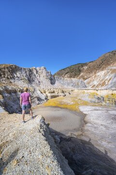 Young tourist at a crater, volcano caldera with pumice fields, yellow coloured sulphur stones, Alexandros crater, Nisyros, Dodecanese, Greece