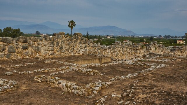 Wide landscape of ruins with stone structures and a palm tree against a blue sky, Tiryns, ancient city in Argolis, Mycenaean, Peloponnese, Greece