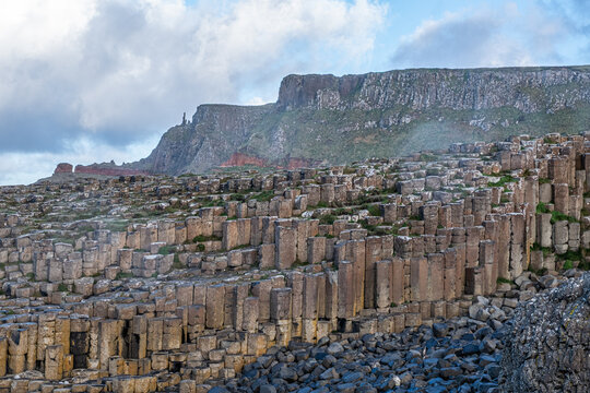 Terraced layers of volcanic basalt columns rising toward high coastal cliffs at the Giant's Causeway