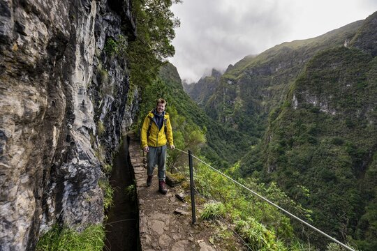 Hikers on a narrow path along a levada, view of forested mountains and gorges, Levada do Caldeir&atilde;o Verde, Parque Florestal das Queimadas, Madeira, Portugal