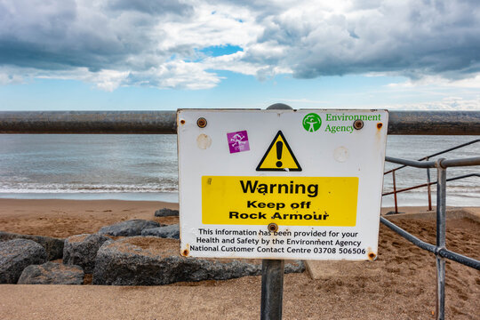 A white and yellow sign attached to railings at Skegness beach in Lincolnshire, UK warns people to keep off rock armour