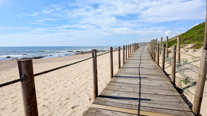 Fototapeta premium Wooden Boardwalk Leading Along the Sandy Coastline of Miramar Beach in Portugal