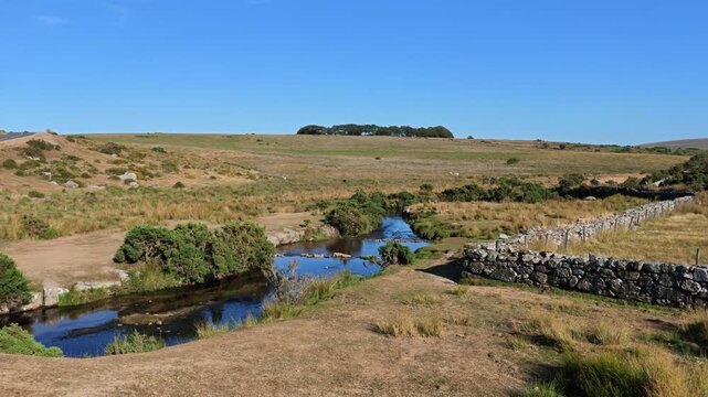 Dartmoor Devon England UK. 13.08.2026. Video. A tranquil rural scene on Dartmoor unfolds with a clear blue sky above the west River Dart and a rustic stone boundary wall