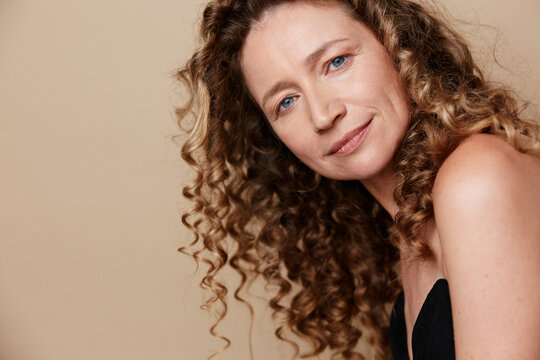 Authentic beauty of a middle-aged woman with natural skin without retouching. Close-up portrait of a smiling female with curly hair showing wellness and self-care concepts.