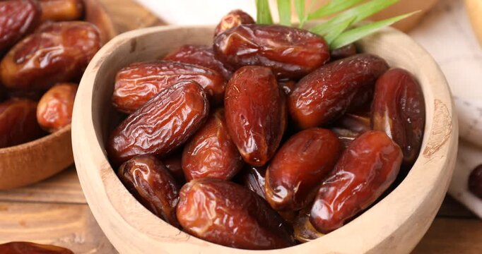 Tasty dried dates and palm leaf on wooden table, closeup. Camera zooming in