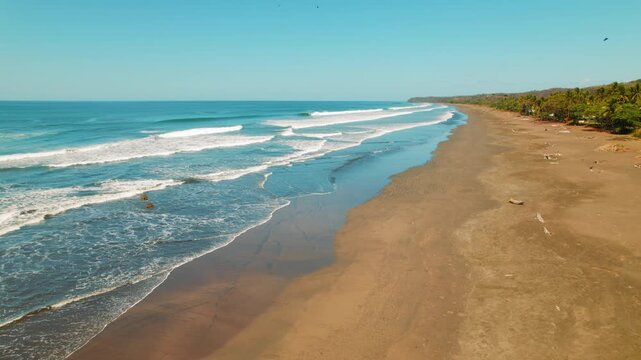 Aerial view of empty sandy beach with rolling waves under blue sky in Costa Rica