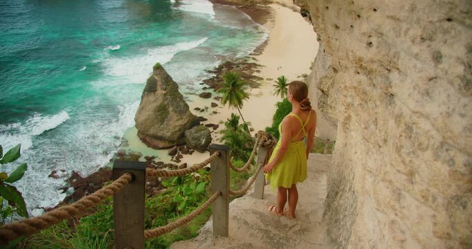 Woman walking stone stairs overlooking ocean and Diamond Beach Nusa Penida Bali Indonesia