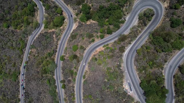 Overhead aerial drone shot panning from left to right over vehicles driving on a winding switchback mountain highway