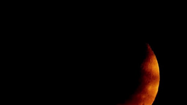 A golden-orange crescent moon with clearly visible crater details in the dark night sky, framed by thin, slowly moving clouds.