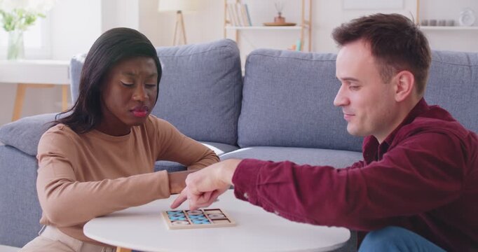 Diverse couple at home playing board games, tabletop with friend, young african american woman and man enjoy play, happy excited homebuyers, property owners amuse new home move, spending good time