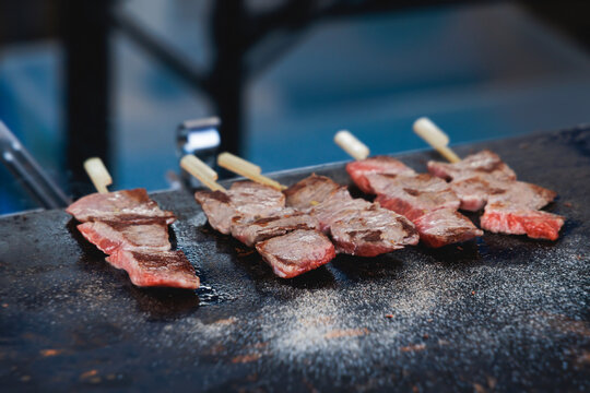 Wagyu beef skewers grilling on hot teppanyaki teppan iron plate, premium Japanese marbled meat on wooden sticks, traditional street food festival, Tokyo, Japan, market with local vendor stalls cooking