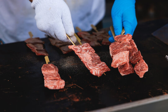 Wagyu beef skewers grilling on hot teppanyaki teppan iron plate, premium Japanese marbled meat on wooden sticks, traditional street food festival, Tokyo, Japan, market with local vendor stalls cooking