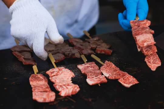 Wagyu beef skewers grilling on hot teppanyaki teppan iron plate, premium Japanese marbled meat on wooden sticks, traditional street food festival, Tokyo, Japan, market with local vendor stalls cooking