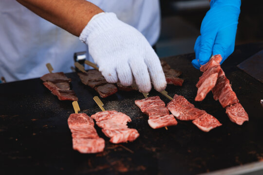 Wagyu beef skewers grilling on hot teppanyaki teppan iron plate, premium Japanese marbled meat on wooden sticks, traditional street food festival, Tokyo, Japan, market with local vendor stalls cooking