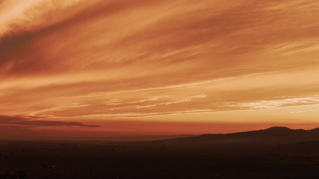 Serene sunset featuring glowing stratus clouds over a dark landscape silhouette. This peaceful, dramatic sky with smooth tracking motion provides an ideal atmospheric cinematic background.