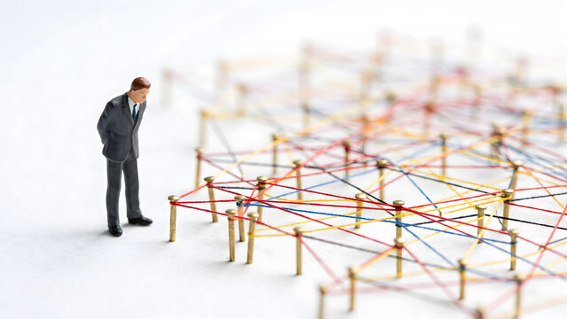 Miniature businessman looking at a complex network of connected colorful strings
