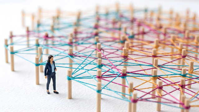 Miniature businesswoman standing next to a complex network of connected wooden pegs