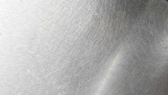 close-up of a scratched metal surface, possibly stainless steel or aluminum. The texture is rough, with numerous fine and deep scratches crisscrossing in various directions, creating a worn and aged