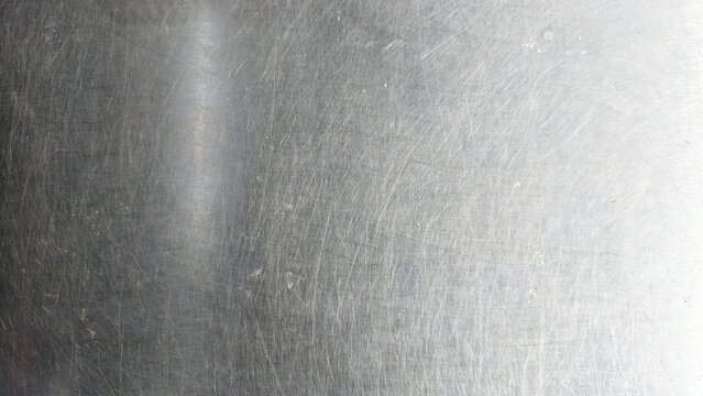 close-up of a scratched metal surface, possibly stainless steel or aluminum. The texture is rough, with numerous fine and deep scratches crisscrossing in various directions, creating a worn and aged