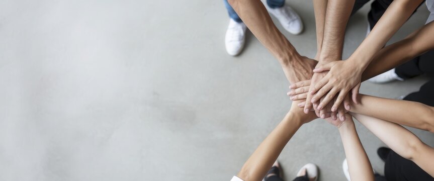 Diverse group of people stacking hands for unity on concrete background.