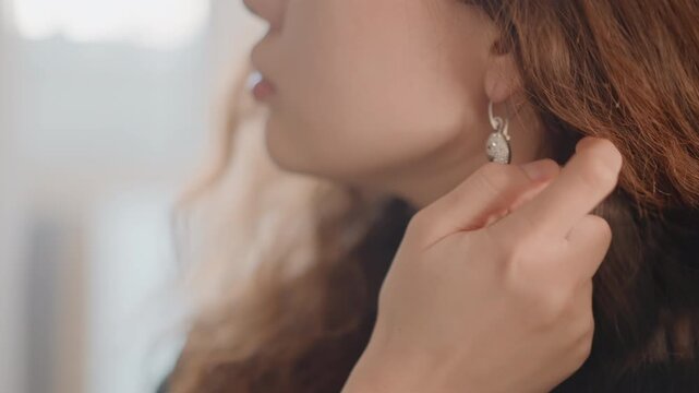 Side-profile close-up of adult woman adjusting dangling geometric earring, then touching neck below ear in soft natural light, showing calm beauty styling, delicate detail, warm tones, and intimate