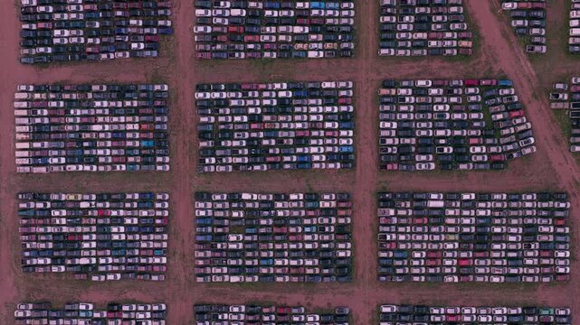 Zenithal aerial forward movement above thousands of parked vehicles arranged in organized rows across a large automotive storage facility.