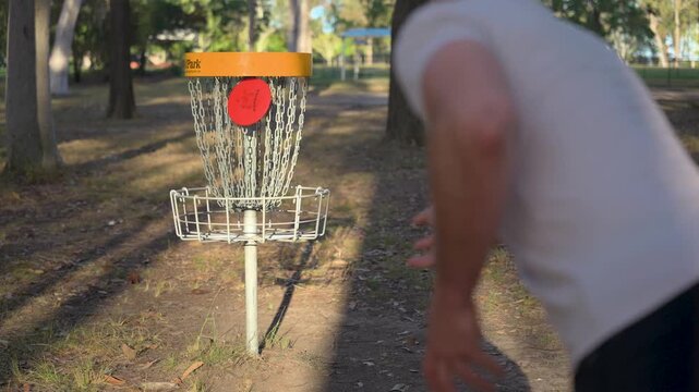 Detail of caucasian man throwing a disc and hitting the net playing disc golf in a public park under trees on a sunny day in Logan, Brisbane, Queensland, Australia.