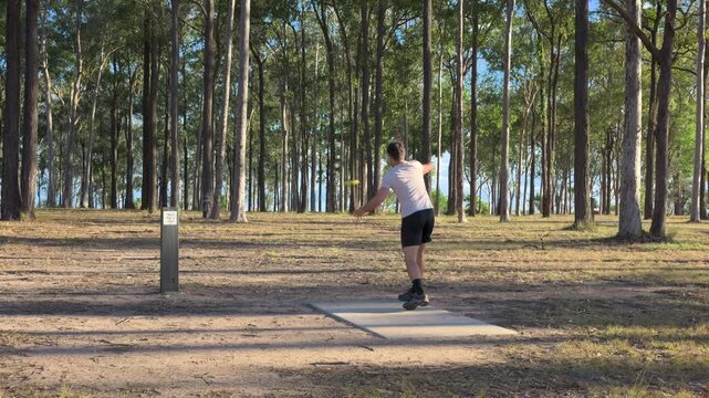 Caucasian man throwing a disc playing disc golf in a public park under trees on a sunny day in Logan, Brisbane, Queensland, Australia.