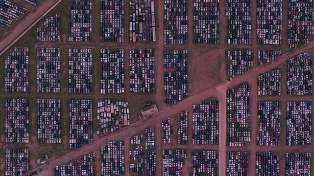Zenithal aerial zoom in over dense geometric rows of parked cars inside a massive vehicle storage and logistics facility.