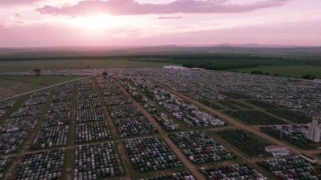 Aerial pan left across a massive automotive storage facility with thousands of vehicles arranged in rows under warm sunset light.