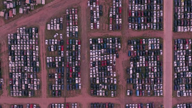 Zenithal aerial pan right across hundreds of vehicles tightly arranged in organized rows inside a large automotive storage facility.