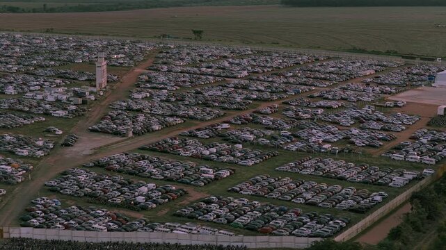 Aerial pan left across dense rows of vehicles inside a massive automotive storage and logistics facility surrounded by rural land.