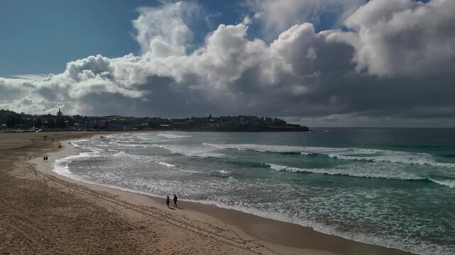 Beach on sunny spring with beautiful clouds and blue sky. People walk along the sand and shore. Camera tracks from R to L