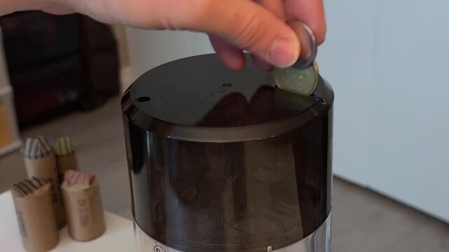 A hand feeding Canadian coins into a coin sorter with coin rolls in the background