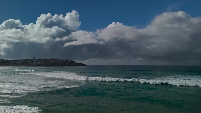Beach on sunny spring with beautiful clouds and blue sky. People walk along the sand and shore. Camera tracks from R to L flying low over surf and waves