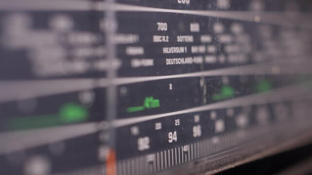 Vintage analog radio tuning scale with frequencies and station names, macro closeup as dial finds correct signal