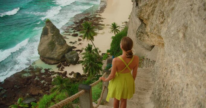 Woman stands on cliffside stairway overlooking Diamond Beach on Nusa Penida island