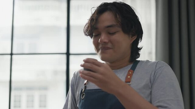 Young man in denim apron pouring freshly brewed coffee from carafe into cup, close-up action shot with soft window light, artisan coffee brewing process and morning ritual concept at home.