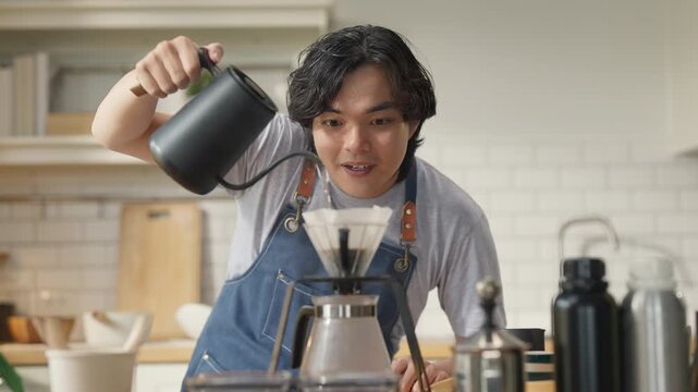 Young man in denim apron pouring freshly brewed coffee from carafe into cup, close-up action shot with soft window light, artisan coffee brewing process and morning ritual concept at home.