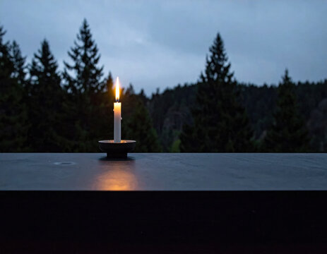 Candle flame forest twilight solitude meditation candle glowing on dark surface before misty evergreen forest at twilight, creating quiet atmosphere of solitude and reflection