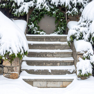 Snowy stone staircase with evergreen wreath and thick winter snow creating quiet festive holiday entrance, showcasing natural decoration and seasonal outdoor architecture