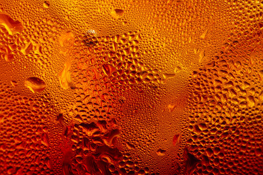 Close-up of condensation water drops on a cold glass of golden beer or beverage,Macro texture background of cold water droplets and condensation covering the surface of a chilled glass with a warm gol
