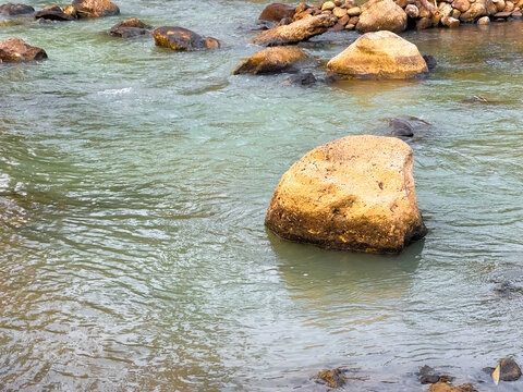 Large boulders in a flowing river stream with gentle ripples and natural scenery
