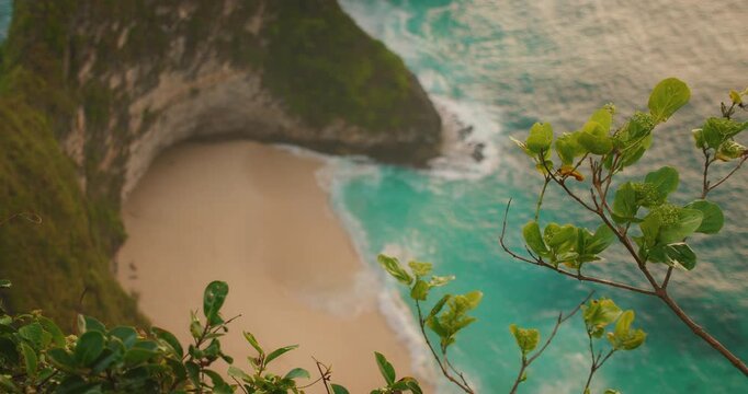 Top down view of turquoise ocean water hitting hidden sandy cove at Kelingking Beach Nusa Penida Bali