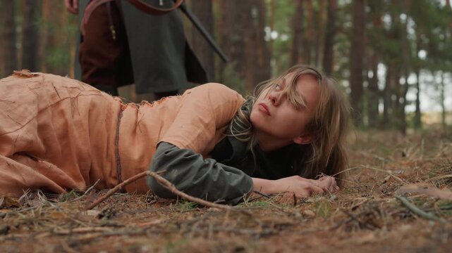 Cloaked figure pulls limp young woman through dense pine forest over uneven ground, with motion blur, urgent struggle, rustic clothing, loose hair, and tense woodland atmosphere, with woman, cloaked