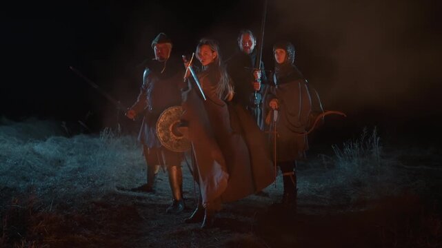 Four armored medieval warriors move forward through low marsh fog under dark night sky; leader steps slightly ahead while cloaks flow, metal armor gleams, and wet ground reflects dim light