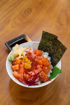 Rice bowl with raw salmon and caviar shrimp roe with seaweed sheets pickled ginger and wasabi on wooden table for traditional healthy and fresh fish to sashimi by Japanese food in seafood restaurant